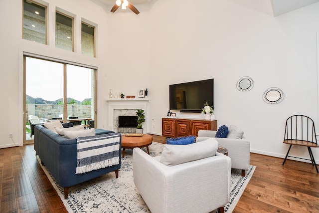 living room featuring wood-type flooring, a towering ceiling, ceiling fan, and a premium fireplace