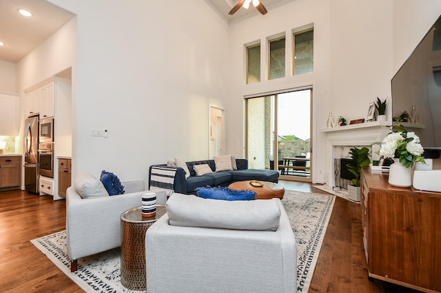 living room with ceiling fan, dark wood-type flooring, and a high ceiling