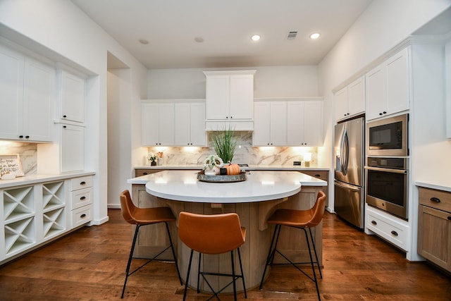 kitchen with a center island, a kitchen breakfast bar, dark hardwood / wood-style flooring, white cabinets, and appliances with stainless steel finishes