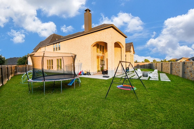 back of house featuring a trampoline, a patio area, and a lawn