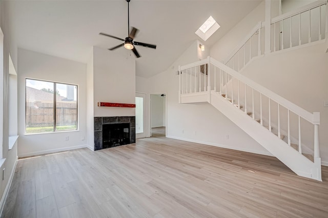 unfurnished living room with a skylight, ceiling fan, high vaulted ceiling, light hardwood / wood-style floors, and a tiled fireplace