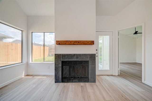 unfurnished living room featuring ceiling fan, light hardwood / wood-style flooring, and a tiled fireplace