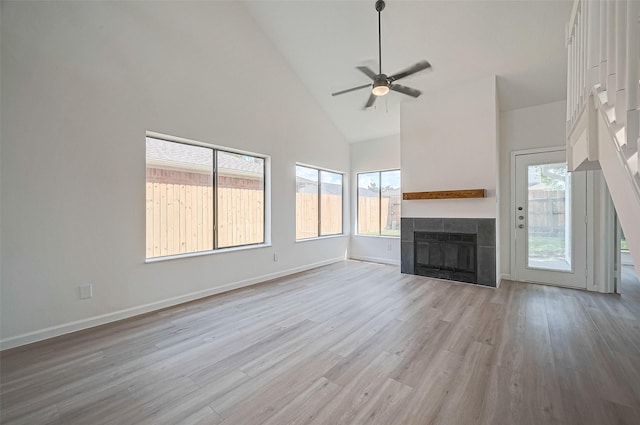 unfurnished living room featuring light hardwood / wood-style floors, high vaulted ceiling, ceiling fan, and a tiled fireplace