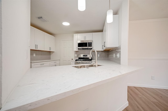 kitchen featuring hanging light fixtures, stainless steel appliances, backsplash, light hardwood / wood-style floors, and white cabinets