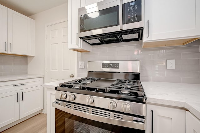 kitchen with light wood-type flooring, appliances with stainless steel finishes, tasteful backsplash, light stone counters, and white cabinetry