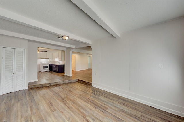 unfurnished living room with beamed ceiling, ceiling fan, light hardwood / wood-style floors, and a textured ceiling