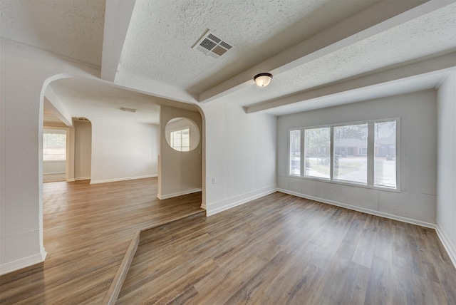 empty room with beam ceiling, a wealth of natural light, and hardwood / wood-style floors