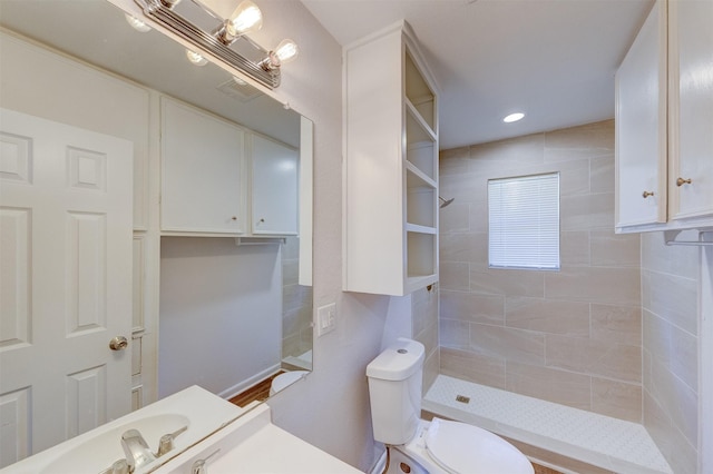 bathroom with a tile shower, vanity, and toilet