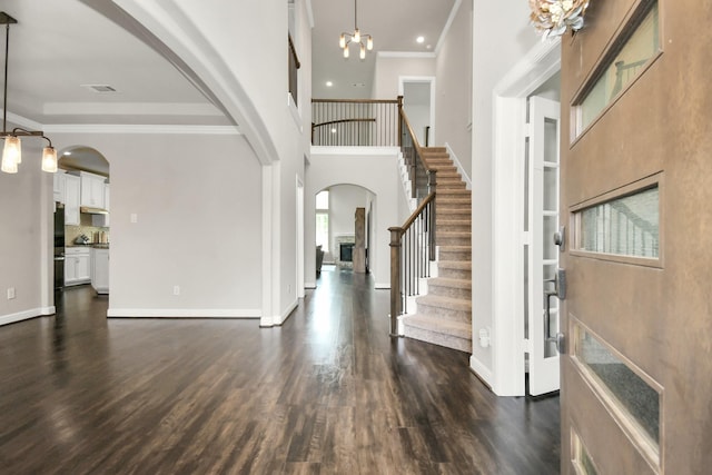 entrance foyer with ornamental molding, dark wood-type flooring, and an inviting chandelier