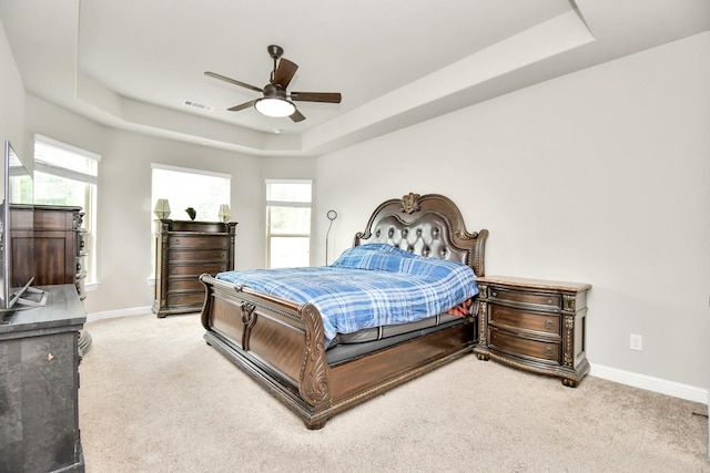 carpeted bedroom with a raised ceiling, multiple windows, and ceiling fan