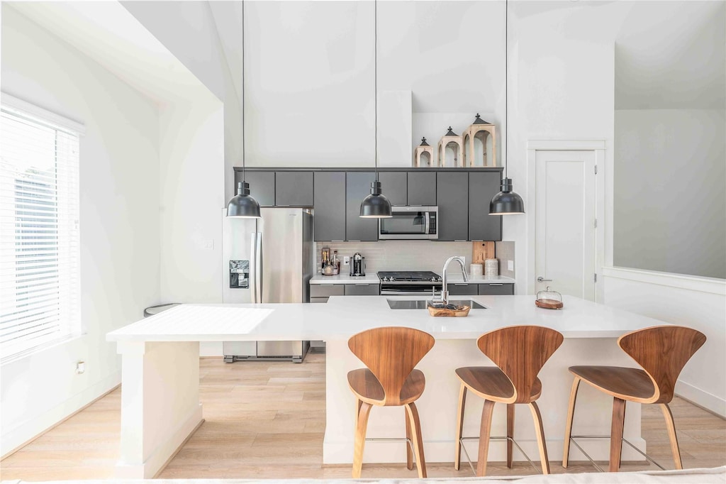 kitchen with light wood-type flooring, tasteful backsplash, a breakfast bar, stainless steel appliances, and sink