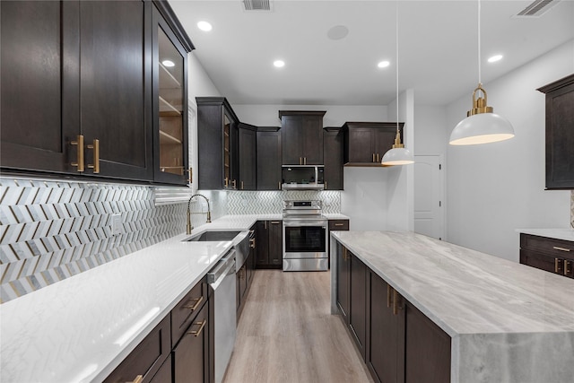 kitchen with sink, light hardwood / wood-style flooring, decorative light fixtures, light stone counters, and stainless steel appliances