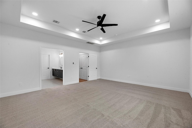 unfurnished bedroom with ensuite bathroom, ceiling fan, light colored carpet, and a tray ceiling