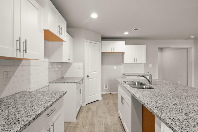 kitchen with light stone countertops, sink, white cabinets, and light hardwood / wood-style flooring