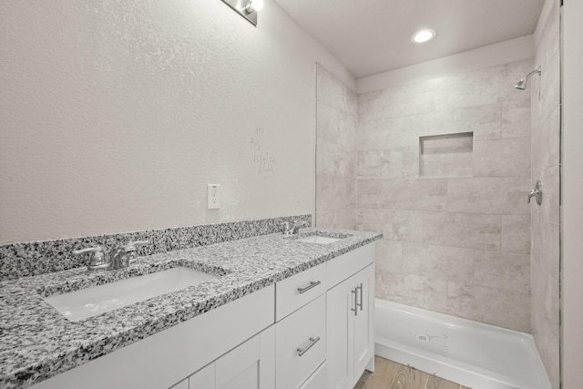 bathroom with hardwood / wood-style flooring, vanity, and tiled shower