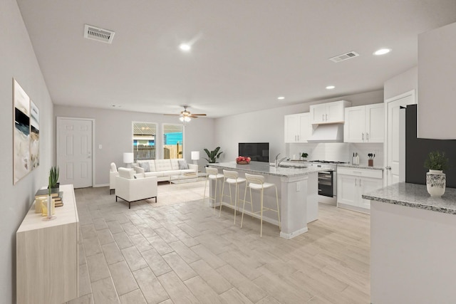 kitchen with white cabinets, light hardwood / wood-style flooring, a kitchen bar, a kitchen island with sink, and high end range