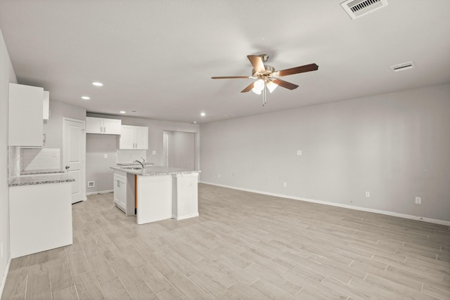 kitchen featuring white cabinets, a center island with sink, light stone countertops, and sink