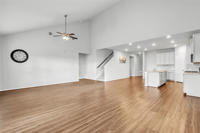 unfurnished living room featuring ceiling fan, sink, high vaulted ceiling, and light hardwood / wood-style floors