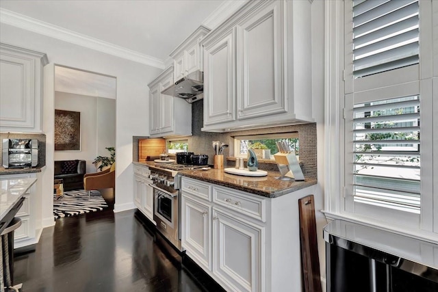 kitchen featuring decorative backsplash, high end stainless steel range oven, crown molding, dark stone countertops, and white cabinetry