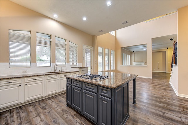 kitchen with sink, stone counters, white cabinets, a center island, and stainless steel gas stovetop