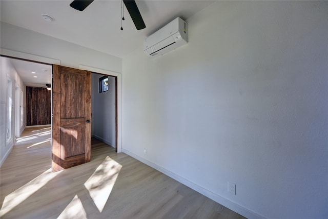 unfurnished bedroom featuring a wall mounted air conditioner, light wood-type flooring, a barn door, and ceiling fan