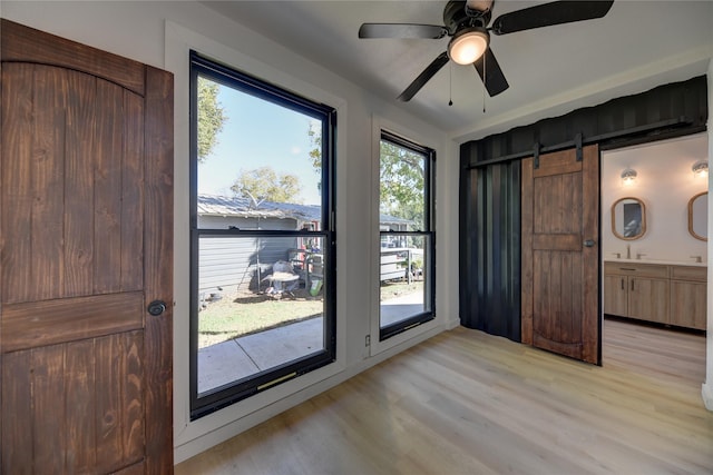 doorway with a barn door, ceiling fan, plenty of natural light, and light hardwood / wood-style floors