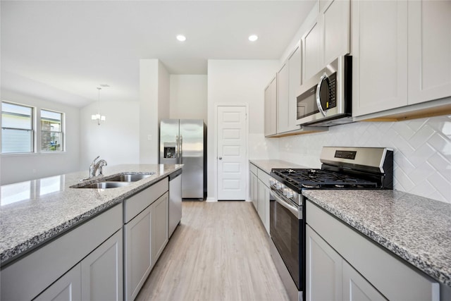 kitchen featuring sink, stainless steel appliances, an inviting chandelier, light stone counters, and light hardwood / wood-style flooring