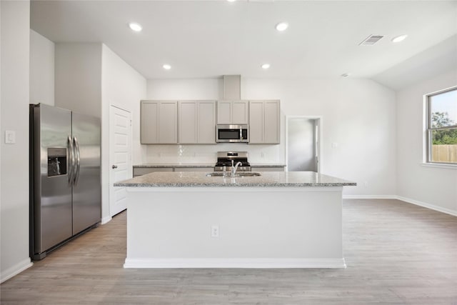 kitchen featuring gray cabinets, light stone counters, stainless steel appliances, and an island with sink