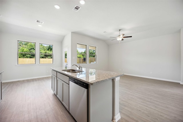 kitchen featuring dishwasher, sink, light stone counters, an island with sink, and lofted ceiling