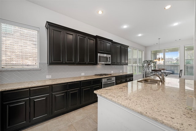 kitchen featuring light stone countertops, tasteful backsplash, stainless steel appliances, sink, and hanging light fixtures