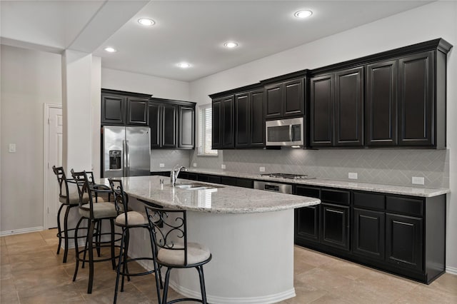 kitchen featuring a kitchen island with sink, a kitchen breakfast bar, sink, appliances with stainless steel finishes, and light stone counters