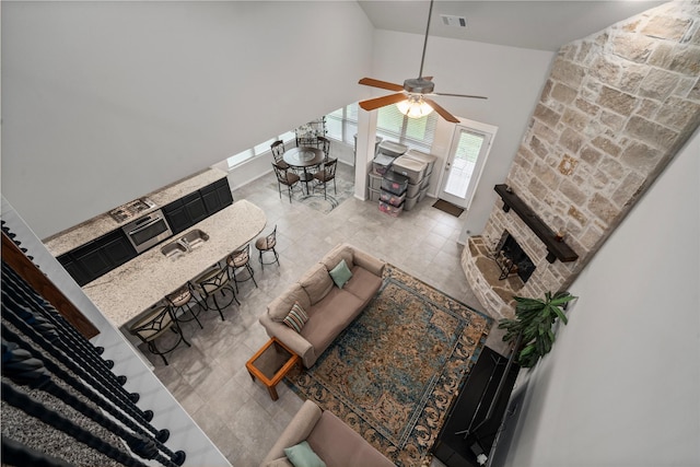 living room featuring ceiling fan, a fireplace, sink, and high vaulted ceiling