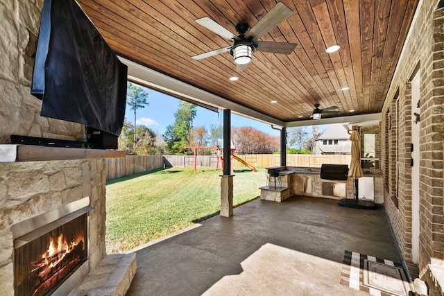 view of patio / terrace with a playground, area for grilling, ceiling fan, and an outdoor stone fireplace