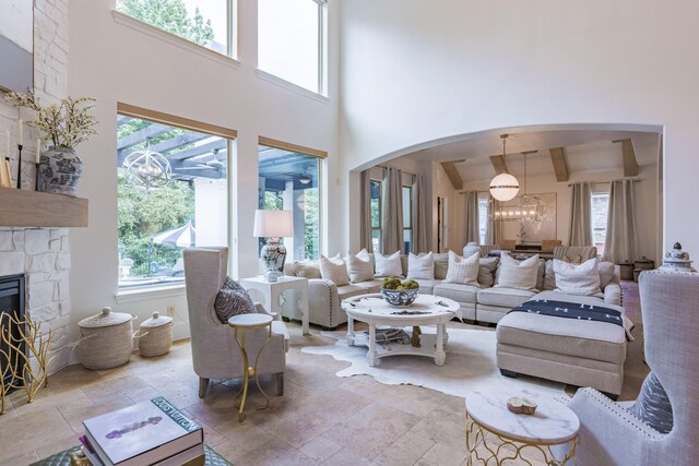 living room featuring a high ceiling, an inviting chandelier, beamed ceiling, and a stone fireplace