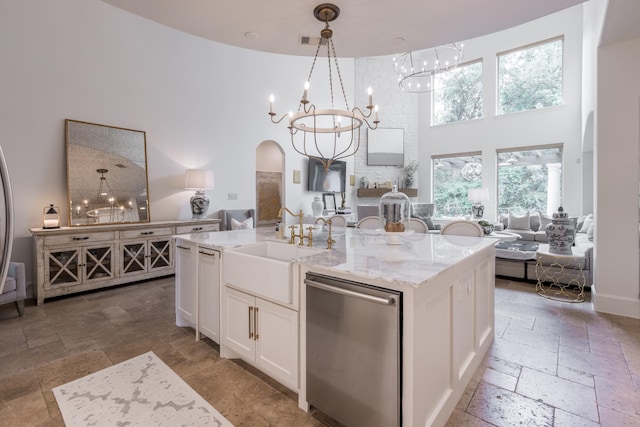 kitchen with an island with sink, stainless steel dishwasher, light stone countertops, and white cabinetry