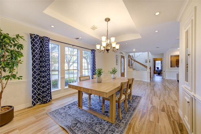 dining area featuring a notable chandelier, a raised ceiling, light wood-type flooring, and a wealth of natural light