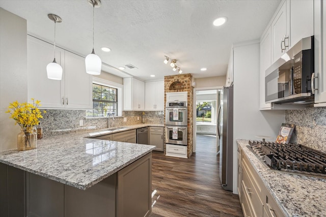 kitchen with white cabinets, decorative backsplash, appliances with stainless steel finishes, decorative light fixtures, and kitchen peninsula