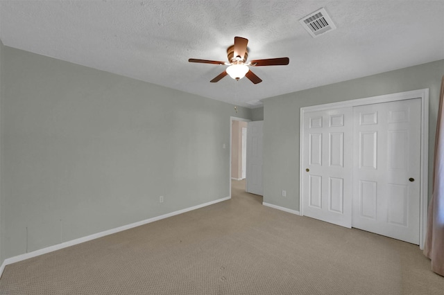 unfurnished bedroom with light carpet, a textured ceiling, a closet, and ceiling fan