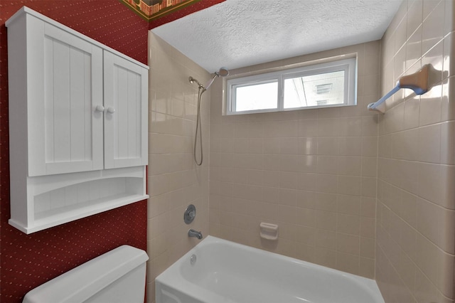 bathroom featuring a textured ceiling, toilet, and tiled shower / bath combo