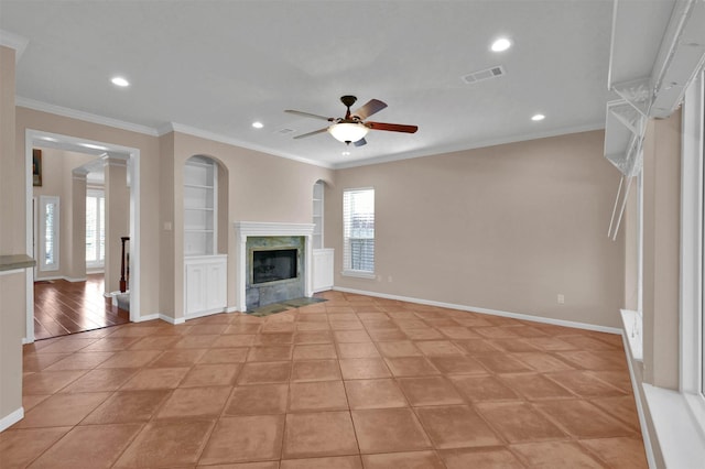 unfurnished living room with built in shelves, ceiling fan, ornamental molding, a fireplace, and light tile patterned floors