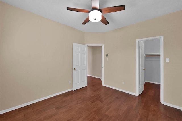 unfurnished bedroom featuring a walk in closet, ceiling fan, a closet, and dark wood-type flooring