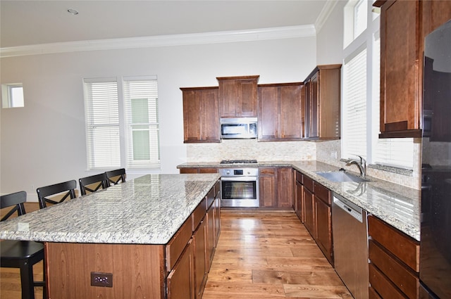 kitchen with a center island, sink, stainless steel appliances, a breakfast bar, and ornamental molding