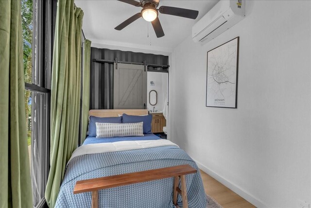 1411 Clay St, Brenham, TX 77833 - bedroom featuring a wall mounted air conditioner, a barn door, wood finished floors, and ceiling fan