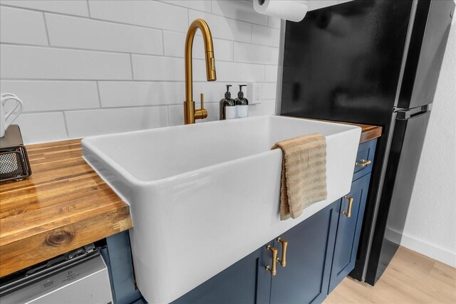 1411 Clay St, Brenham, TX 77833 - detailed view of blue cabinetry, tasteful backsplash, light wood-type flooring, and freestanding refrigerator