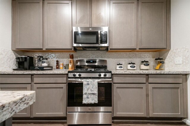 kitchen featuring light stone countertops, stainless steel appliances, gray cabinets, and decorative backsplash