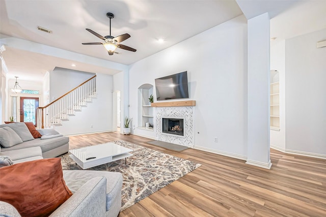 living room featuring hardwood / wood-style flooring, ceiling fan, built in features, and a fireplace