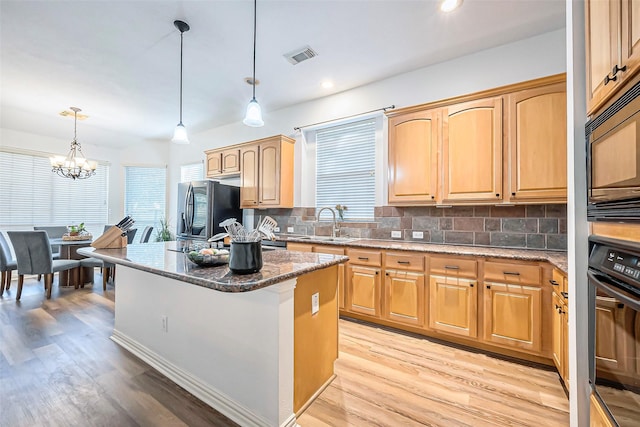 kitchen with an inviting chandelier, dark stone countertops, pendant lighting, a kitchen island, and black appliances