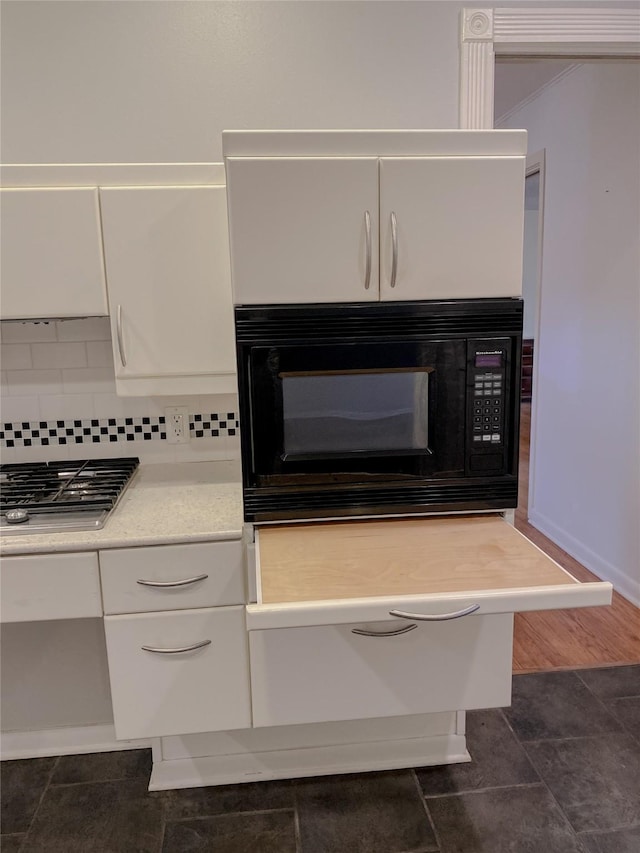 interior details featuring black microwave, light countertops, white cabinets, and decorative backsplash