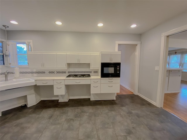 kitchen with stainless steel gas stovetop, black microwave, tasteful backsplash, sink, and white cabinets