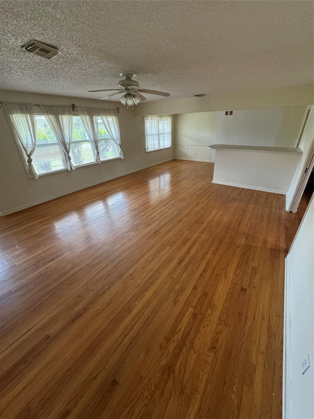 interior space featuring baseboards, visible vents, a ceiling fan, wood finished floors, and a textured ceiling